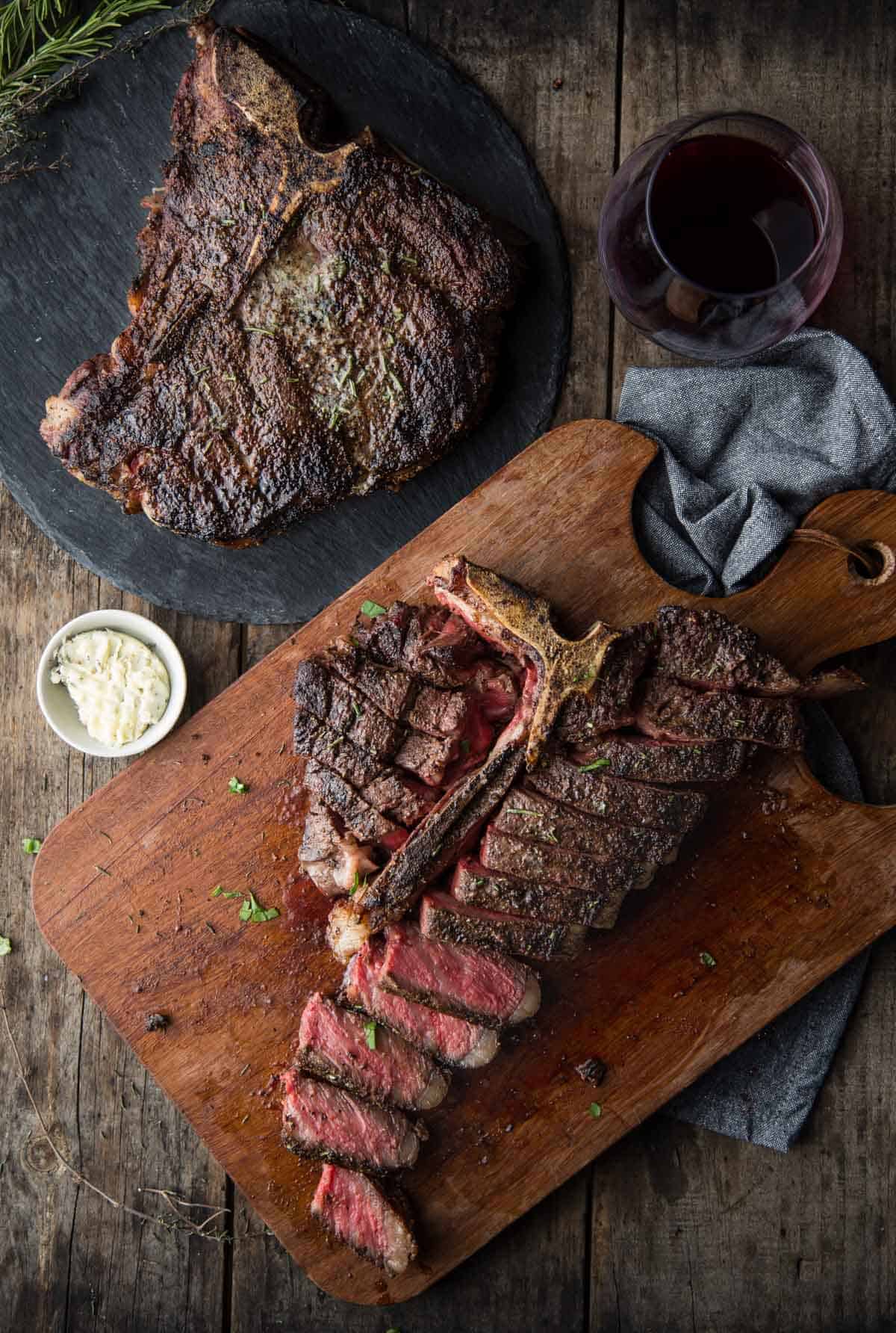 Two Grilled T-Bone Steaks on a cutting board with a glass of wine