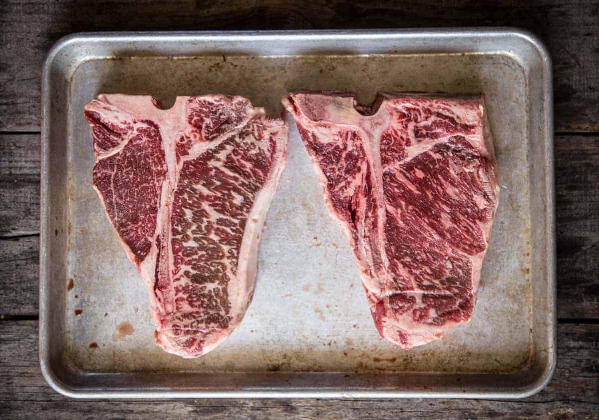 A side by side photo with the porterhouse steak on the left and the t-bone on the right with the smaller beef tenderloin.