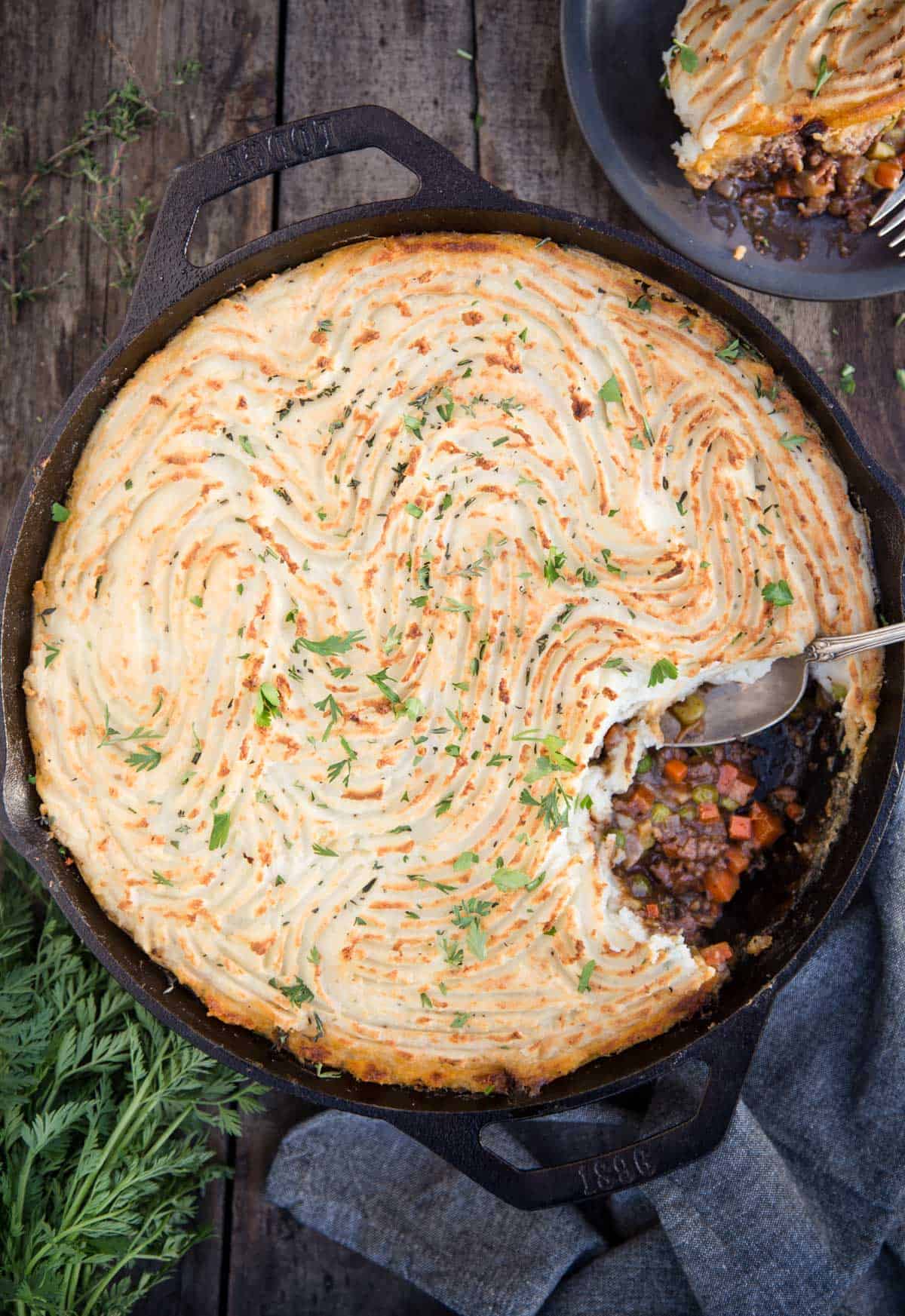A cast iron pan filled with Grilled Shepherd's Pie on a wood table.