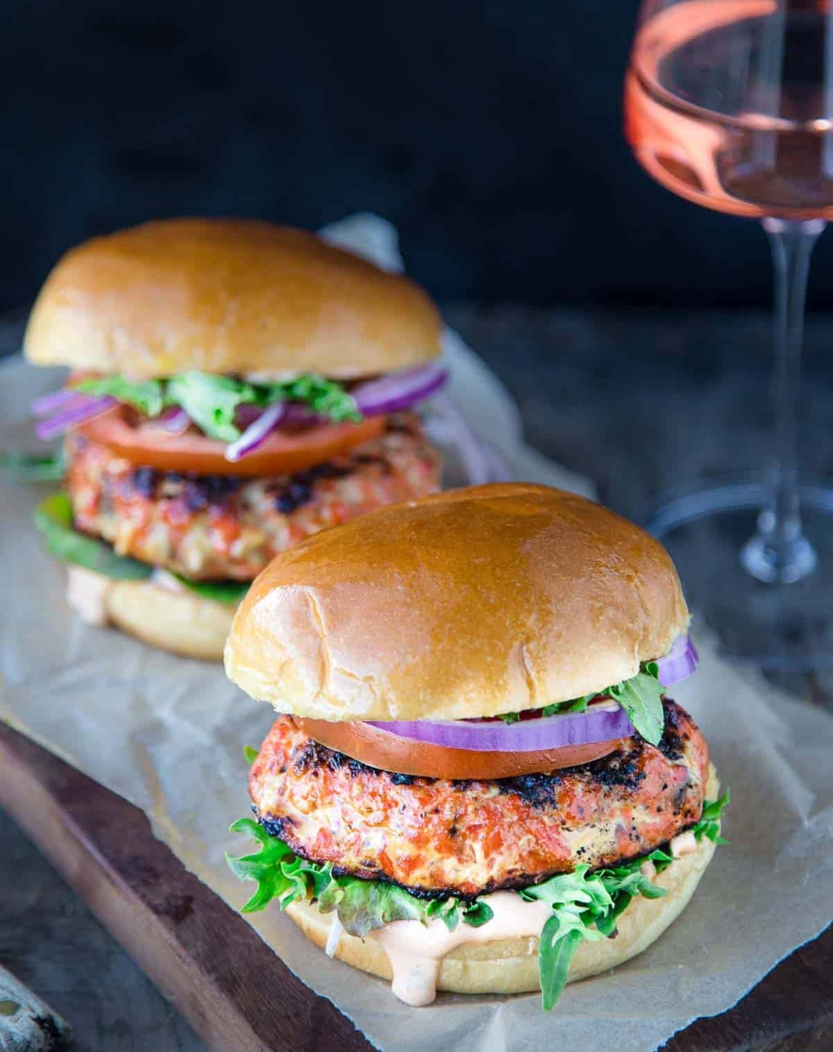 Two grilled salmon burgers topped with a Chipotle lime mayo with a glass of rosé wine next to them.