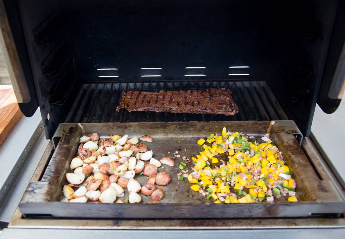 Vegetables and steak cooking on the grill at the same time, preparing for breakfast burritos.