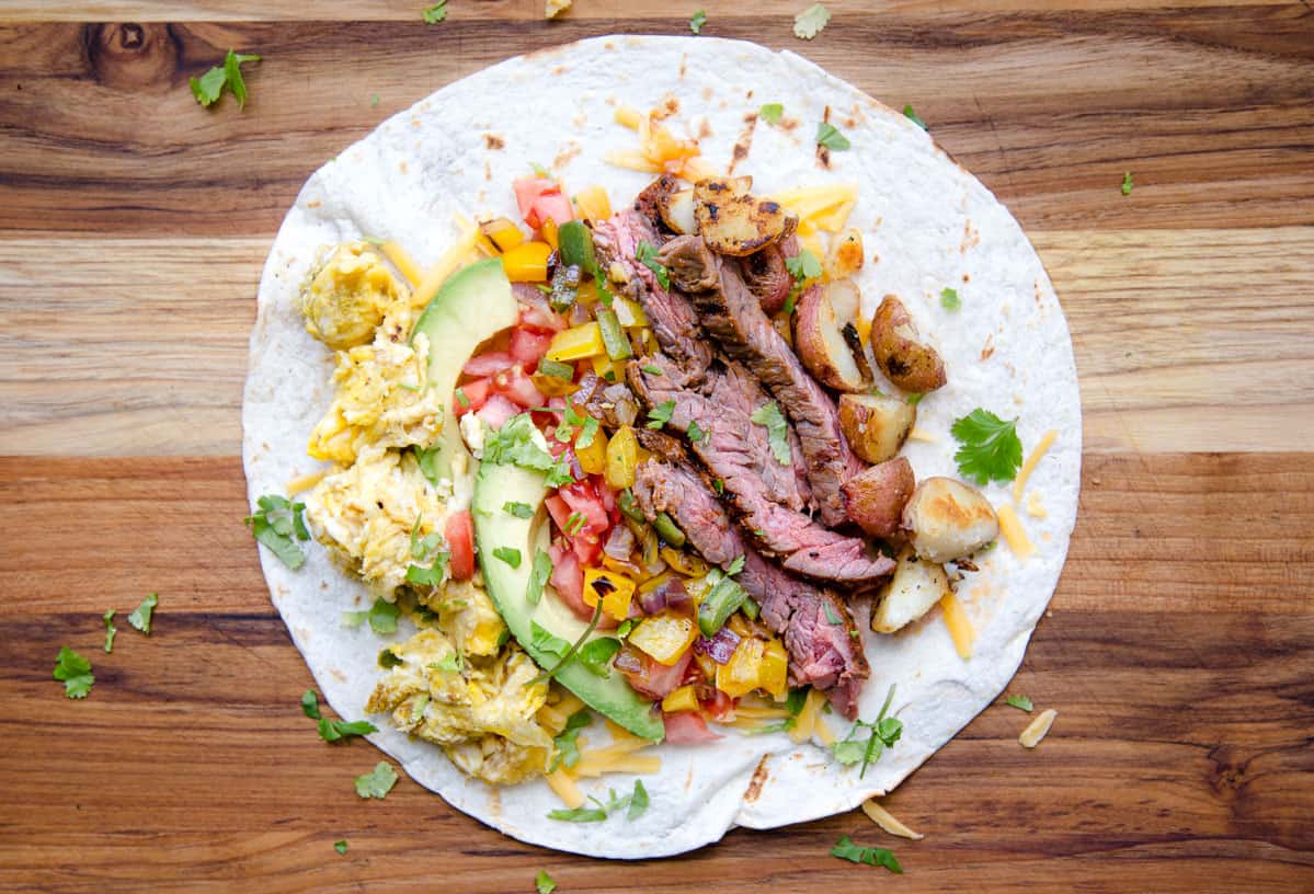 An open faced breakfast burrito filled with steak, vegetables, and eggs before being wrapped. 