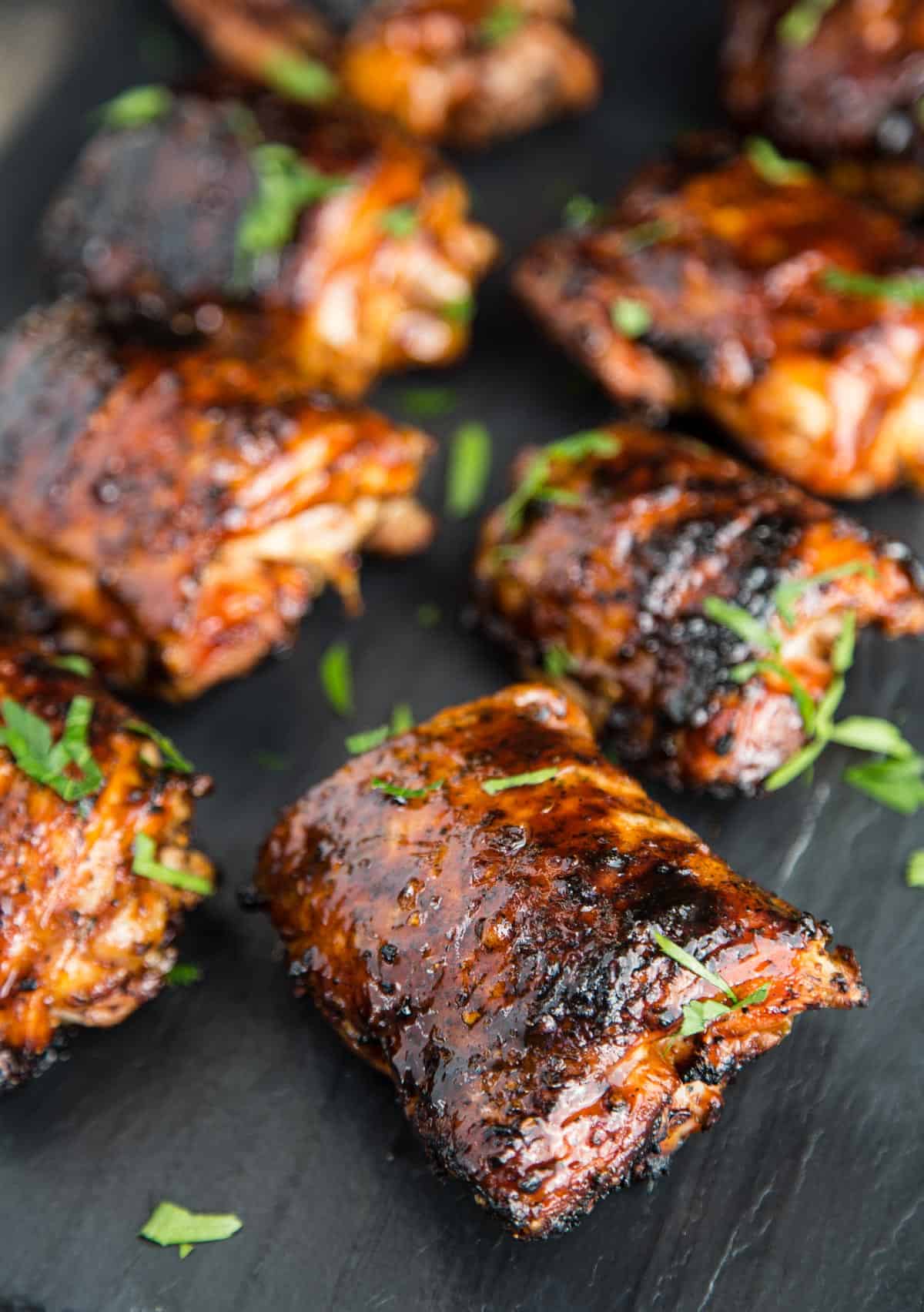 A closeup of grilled chicken thighs on a black platter after being topped with BBQ sauce