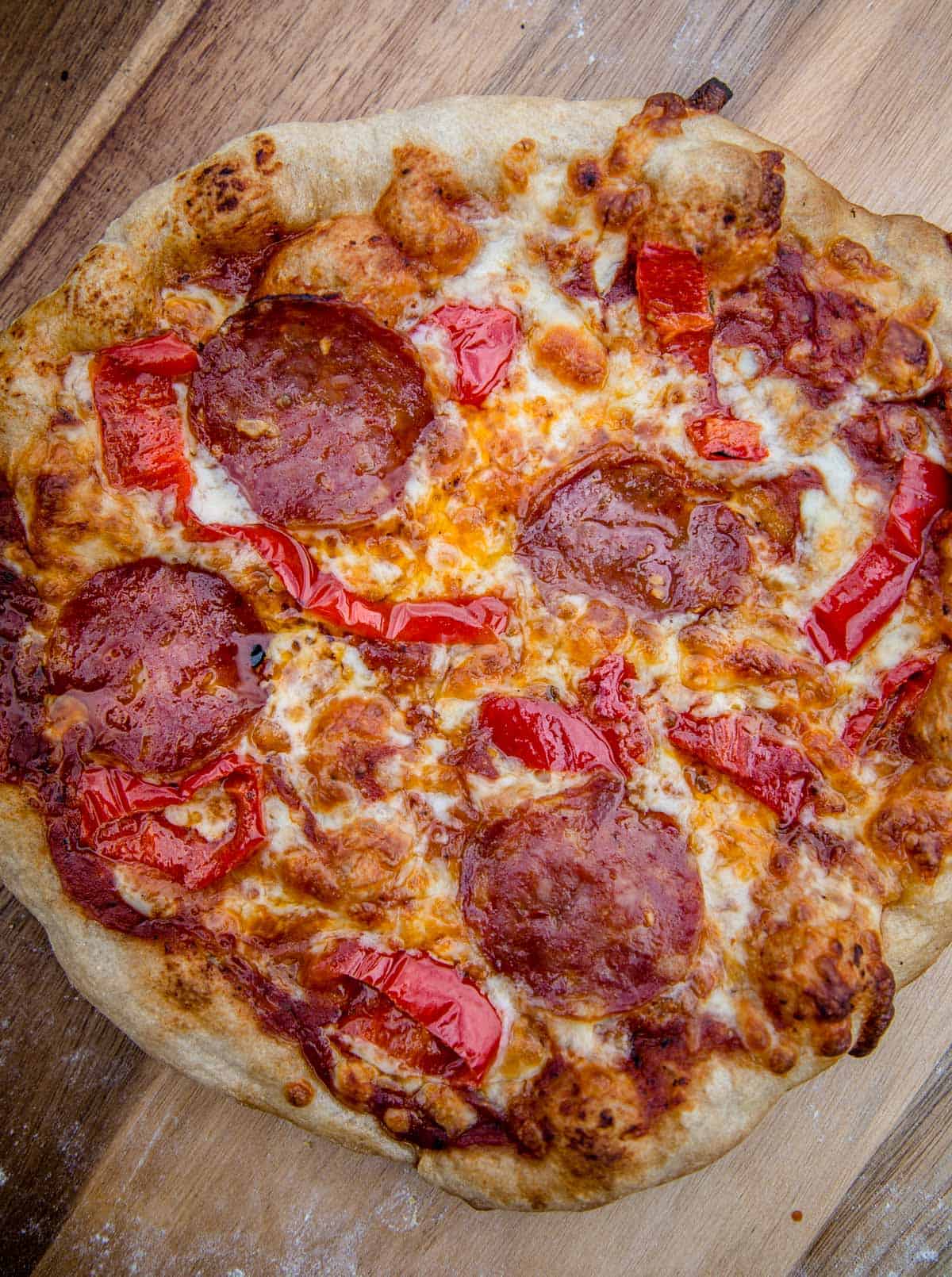 A pepperoni and hot pepper pizza that was cooked on the grill