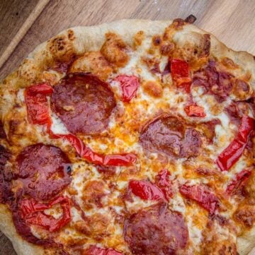 A big green egg baked pizza on a cutting board with salami and hot peppers.