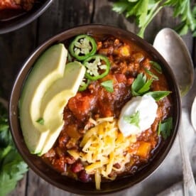 A bowl of beef chili topped with sour cream, avocado, and jalapeño