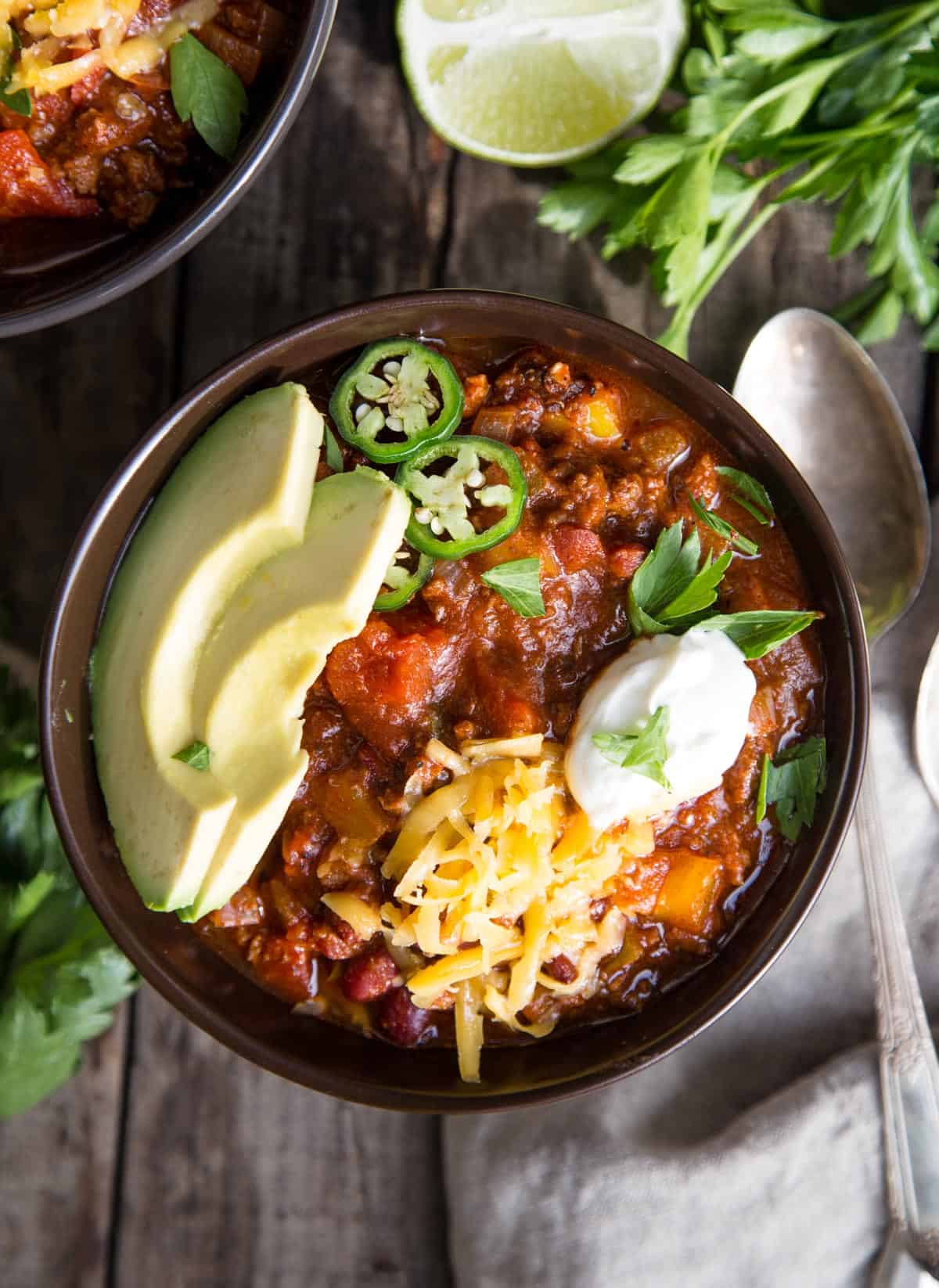 A bowl of beef chili topped with sour cream, avocado, and jalapeño