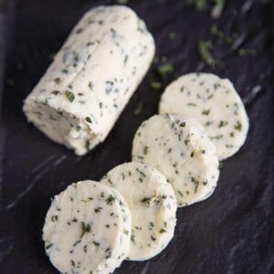 Herb Compound Butter log cut into slices on a black platter