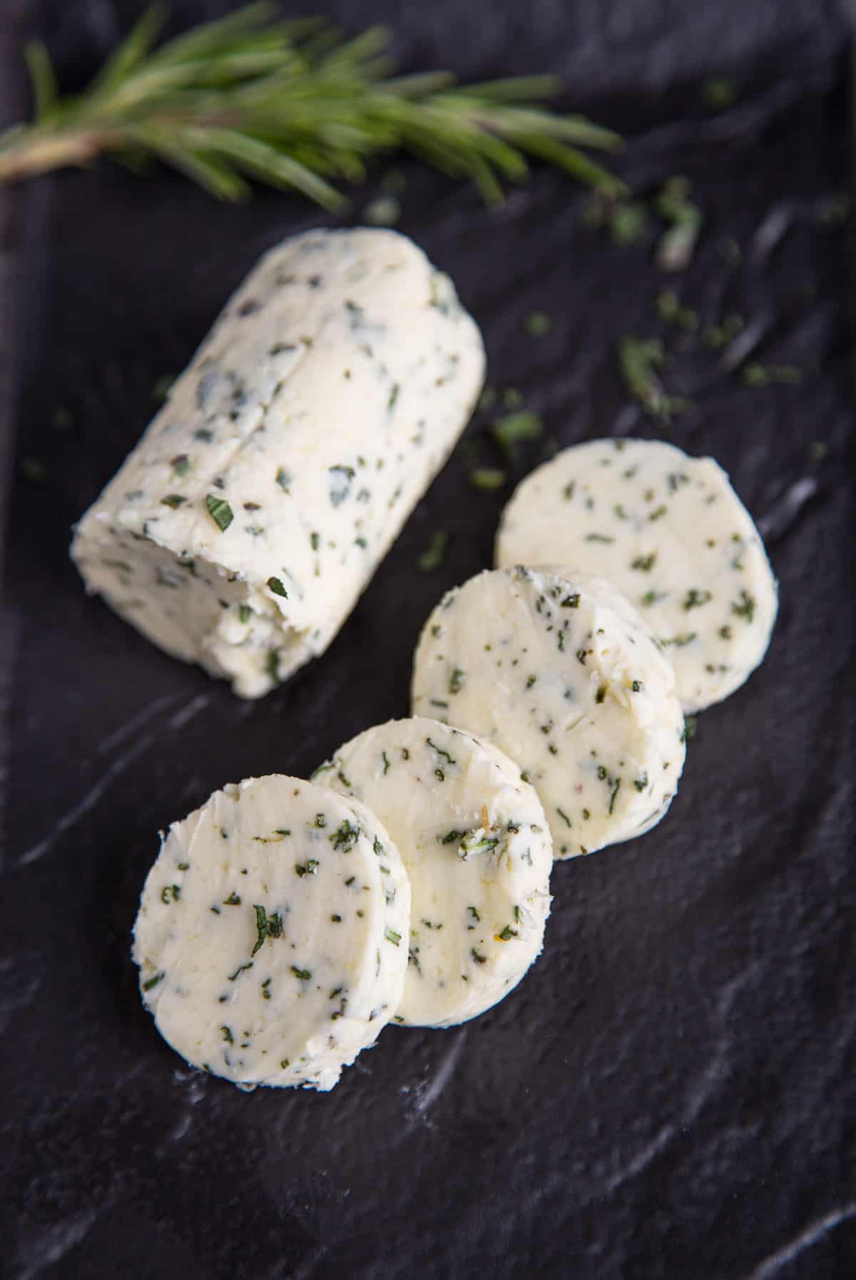 A log of herb compound butter, sliced into rounds on a black platter