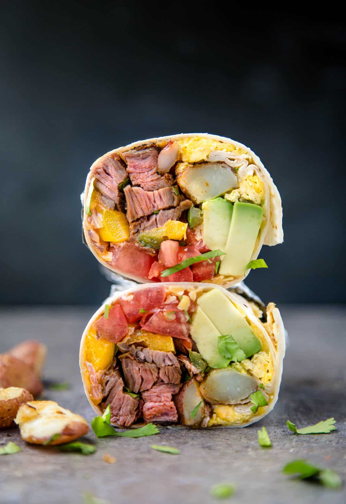 A burrito filled with steak, vegetables, and eggs, cut in half.