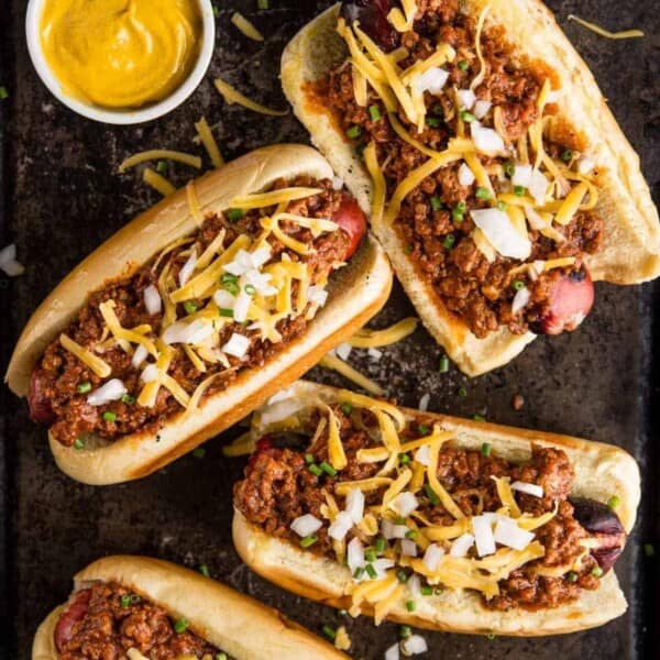 Chili dogs in buns on a cutting board with mustard.