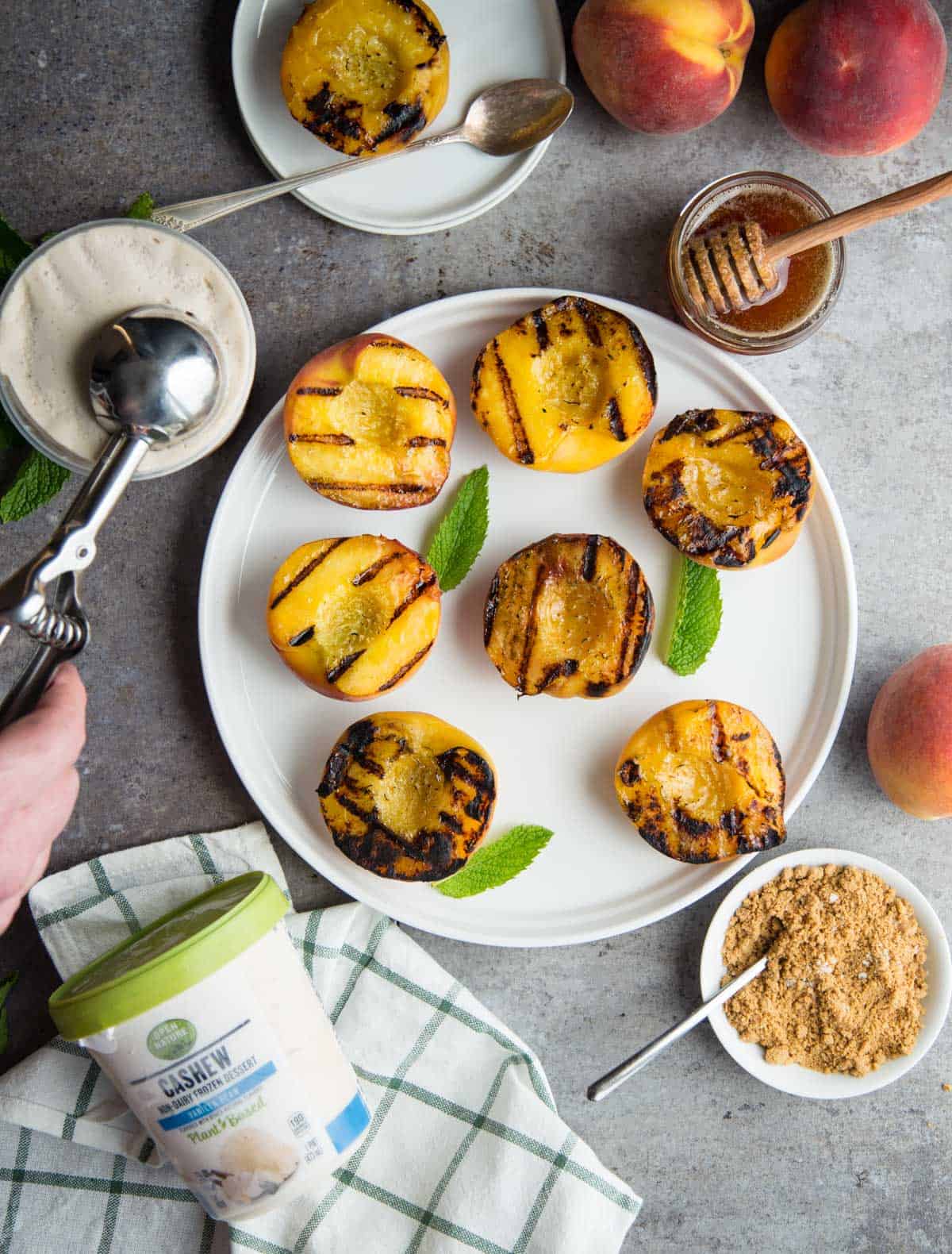 Grilled Peaches on a platter with a hand scooping ice cream