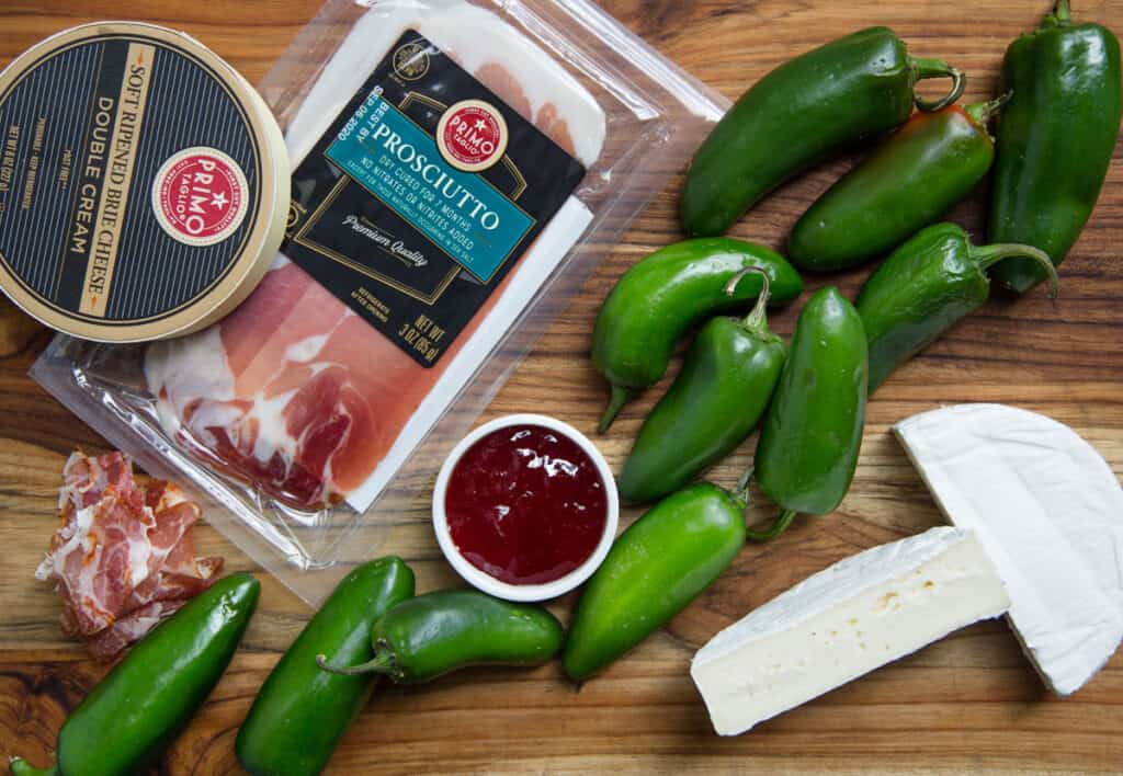 Ingredients for jalapeno poppers with brie cheese and prosciutto on a wood cutting board