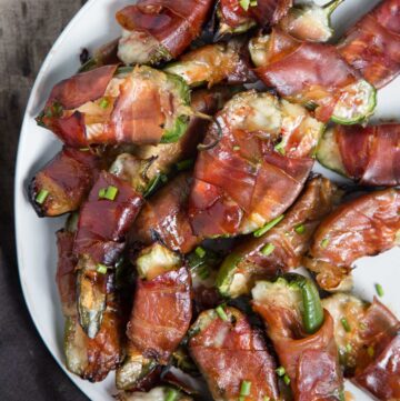 A platter of jalapeño poppers stuffed with brie cheese and wrapped with prosciutto on a white plate