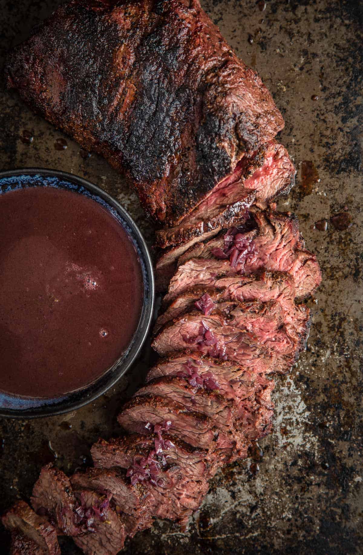 A grilled Tri Tip on a platter, sliced into thin strips, and topped with a red wine reduction sauce.