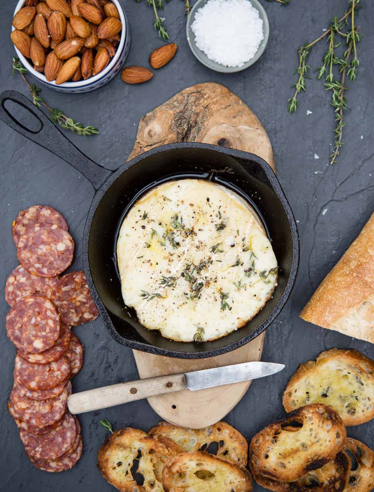 A cheese board with grilled brie, baguette slices, almonds, and salami