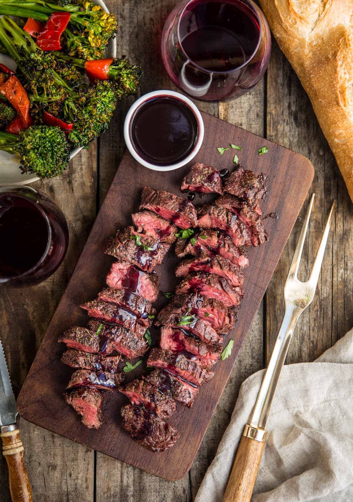 Grilled Hanger Steak on a wood serving platter covered in a wine reduction sauce and two glasses of wine