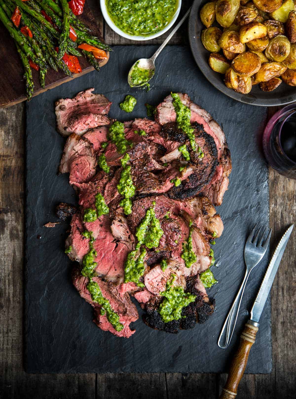 Grilled Picanha Steak sliced and topped with chimichurri sauce on a black slate platter 