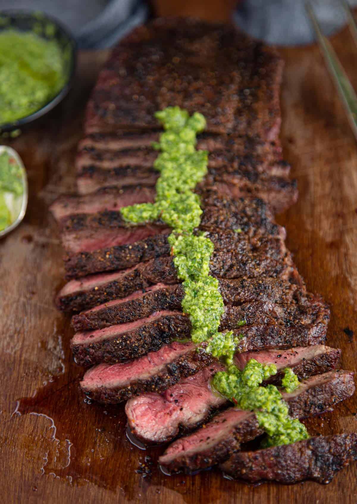 Slices of grilled flat iron steak topped with chimichurri sauce.