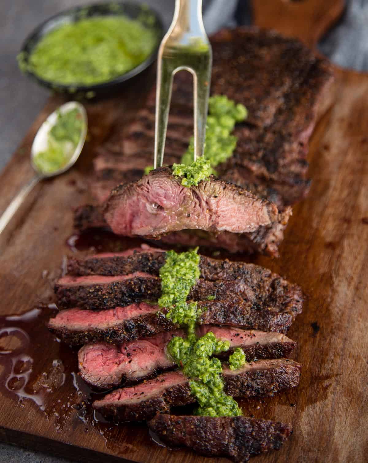 Sliced grilled flat iron steak with jalapeno chimichurri sauce over the top.