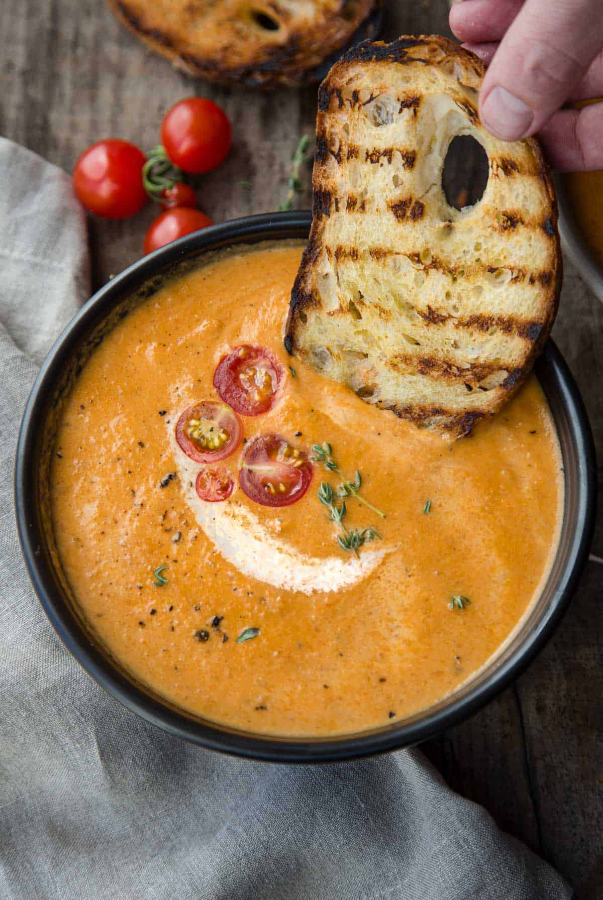 A bowl of smoked tomato bisque and toasted bread dipping into the soup