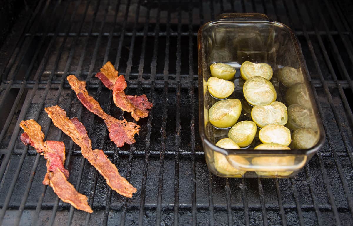 A bowl of tomatillos and 4 pieces of bacon cooking on a smoker