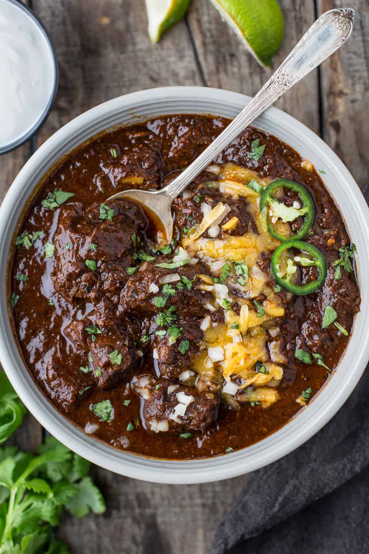 A bowl full of Texas Chili topped with shredded cheese, onions, and jalapeño 