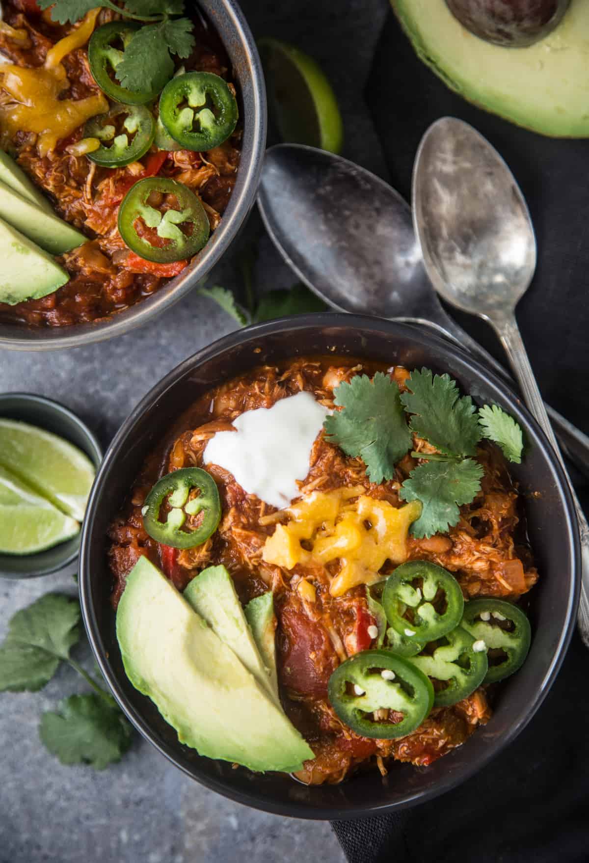 Two bowls full of smoked chicken chili topped with chili toppings