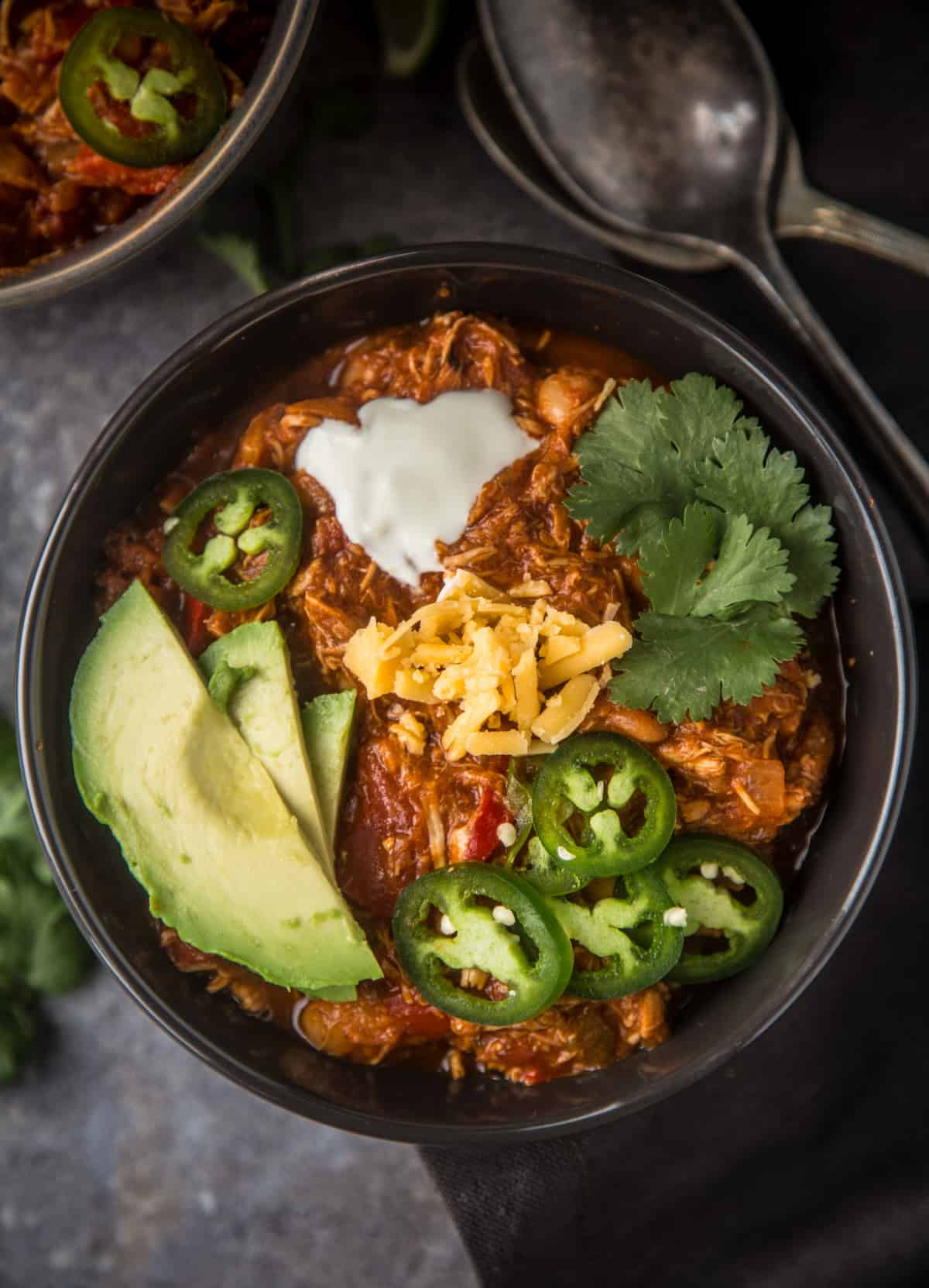 A bowl of easy smoked chicken chili topped with avocado, cheese, and jalapeño 