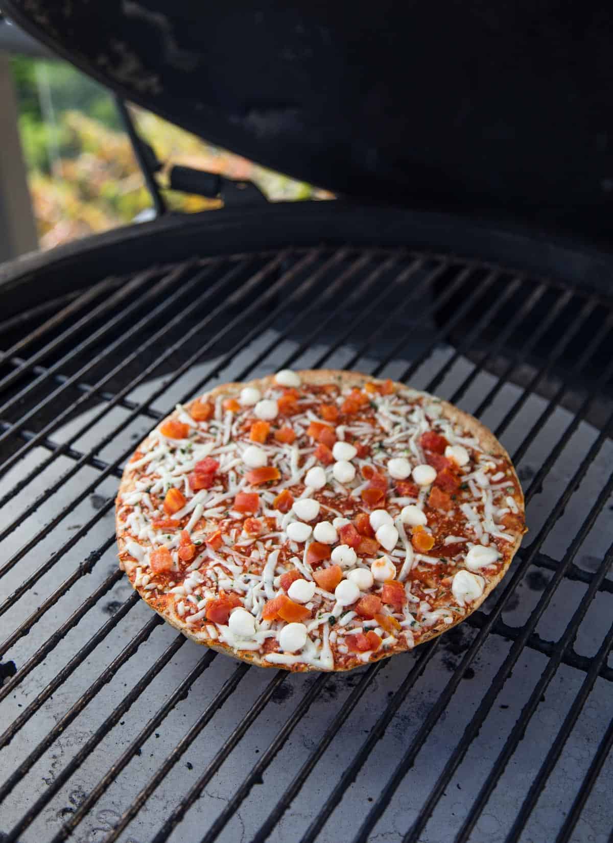A frozen pizza cooking on a grill