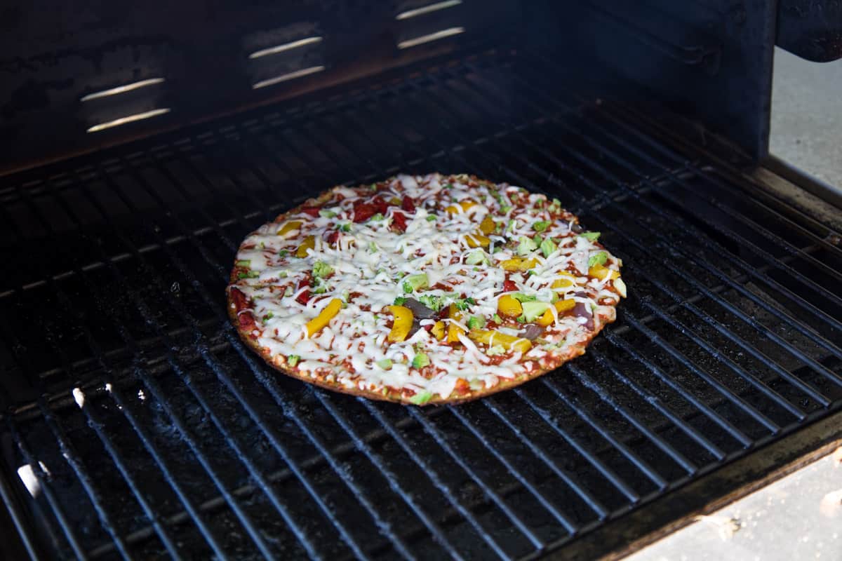 A frozen pizza cooking on a pellet grill