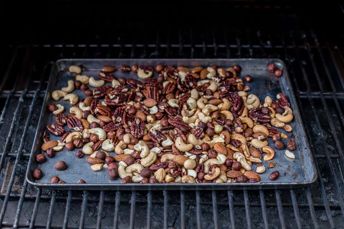 Mixed nuts on a sheet pan in a pellet smoker for holiday nuts.