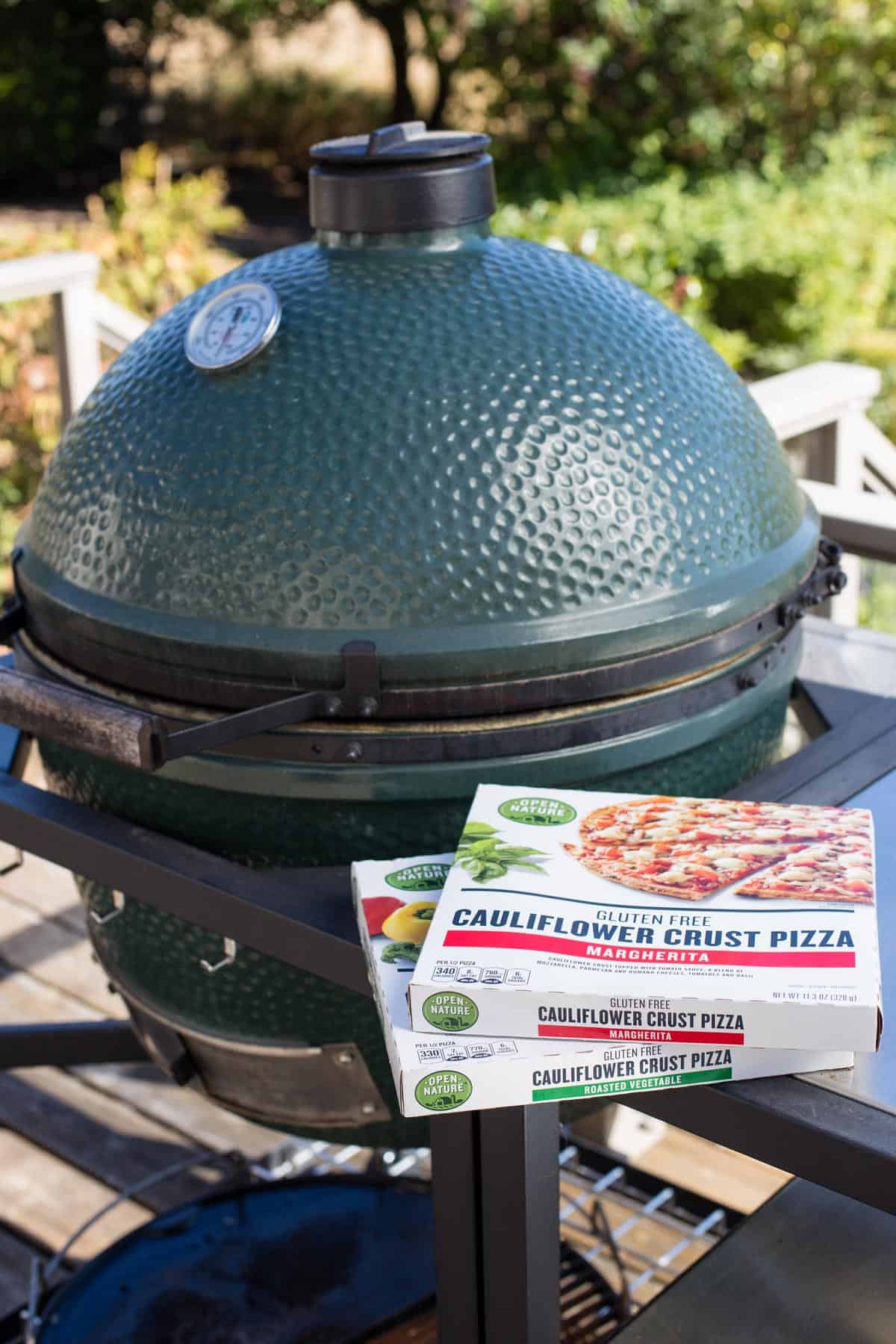 Two frozen pizzas right next to a Big Green Egg grill