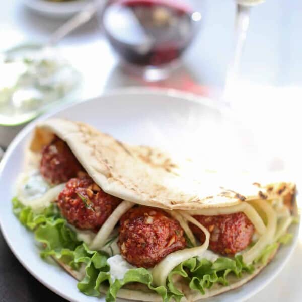 Smoked Lamb Meatball Pita on a plate with a glass of wine