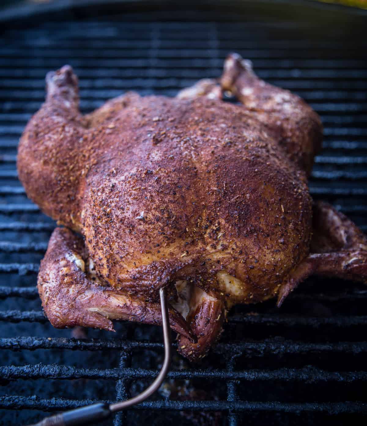 A whole chicken cooking on a smoker
