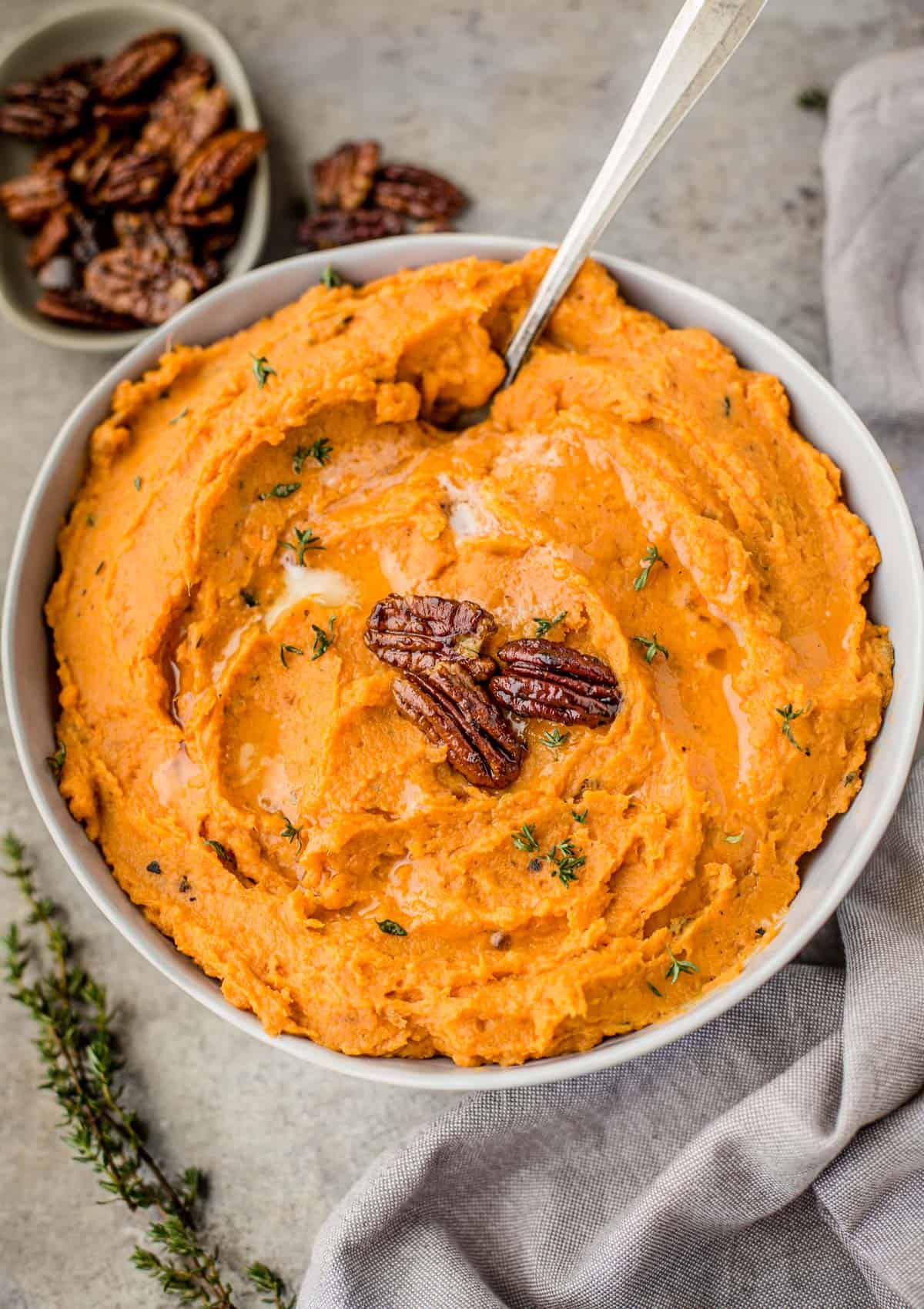A bowl willed with mashed sweet potatoes topped with candied pecans.