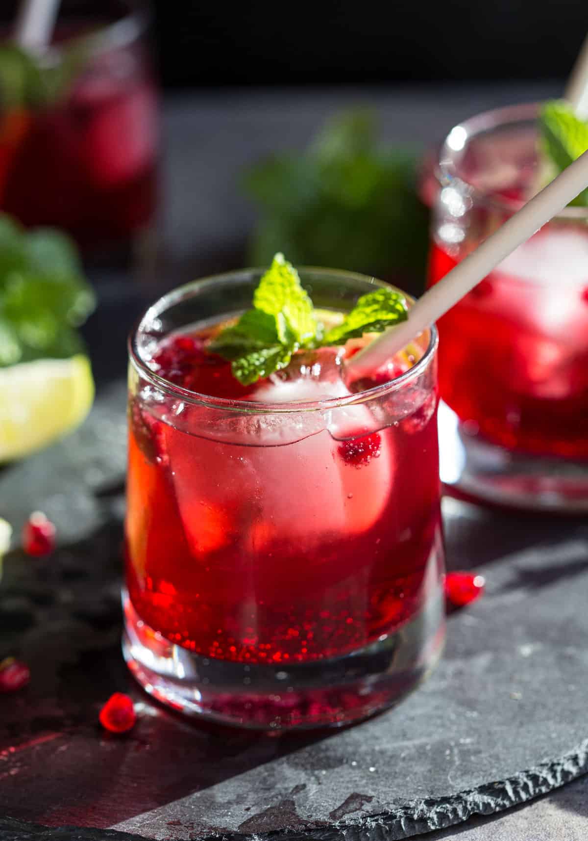 Ginger Pomegranate Spritz cocktail in a glass with a straw and fresh mint garnish