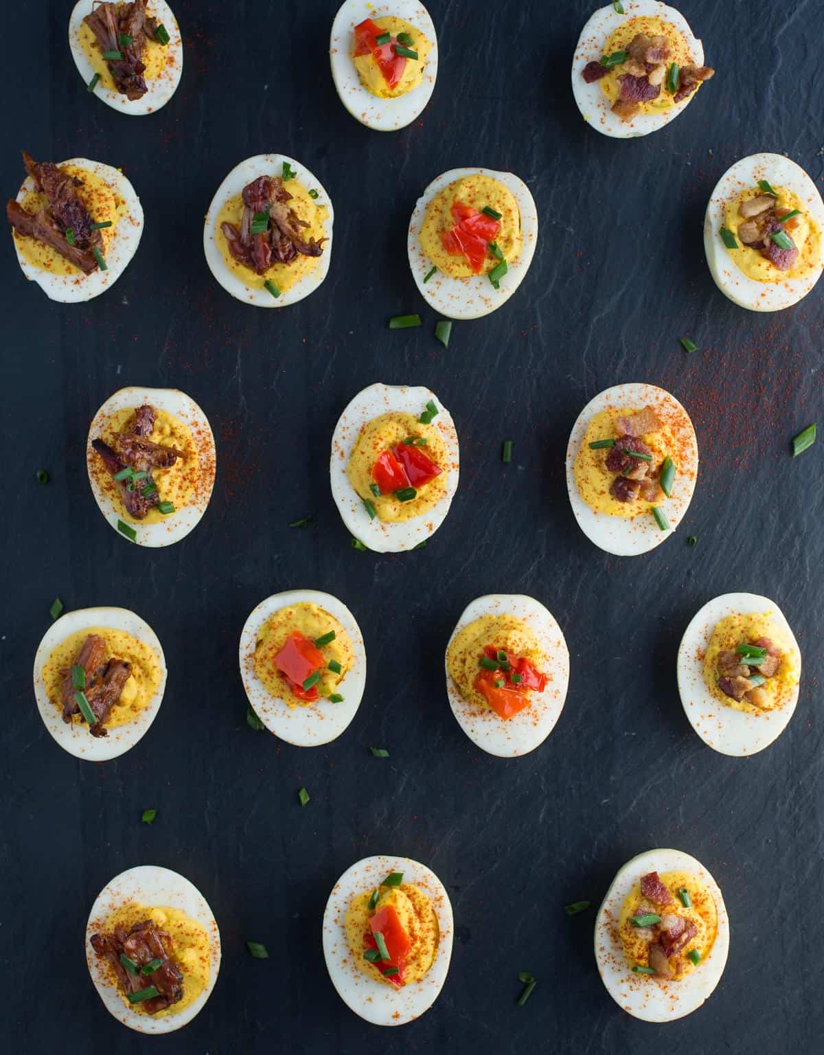 A platter full of smoked deviled eggs topped with brisket, pickled peppers, and crispy bacon
