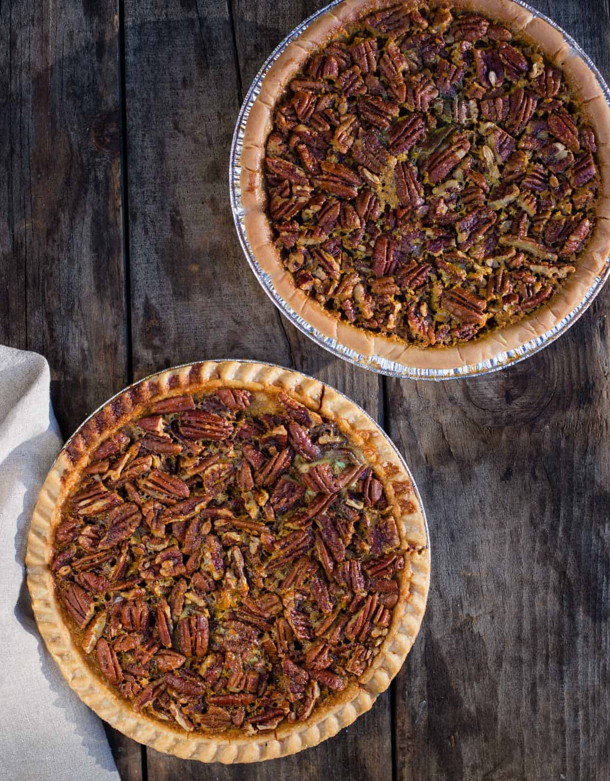 Two pecan pies resting on a wood board