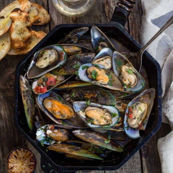 Grilled Mussels in a cast iron pan with broth and toasted bread.