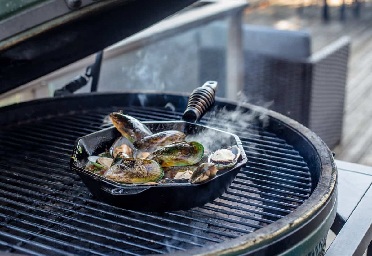A cast iron pan filled with mussels on the hot grill.