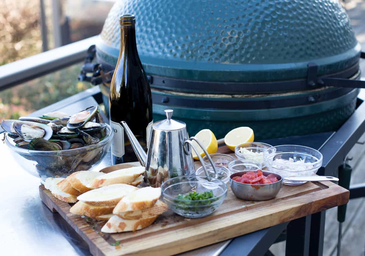 Ingredients for grilled mussels on a cutting board next to the grill.