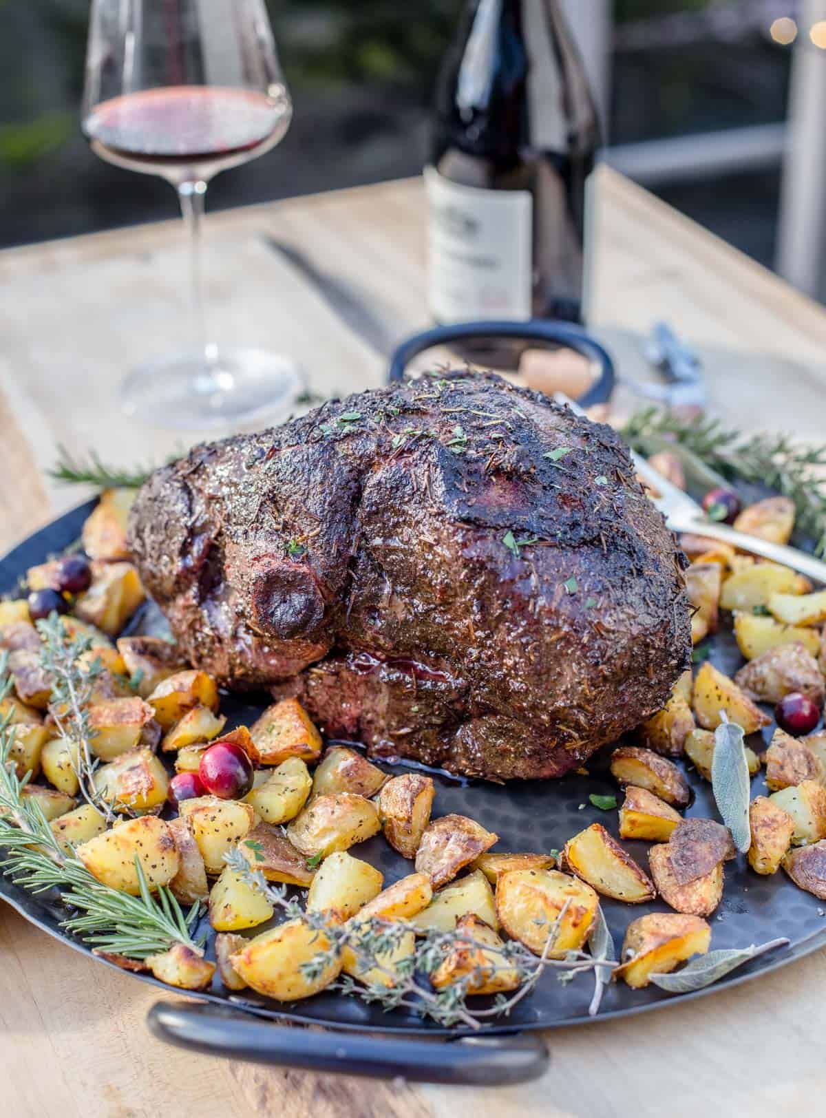 A smoked leg of lamb on a platter with roasted potatoes