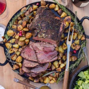 A smoked leg of lamb on a platter with roasted potatoes