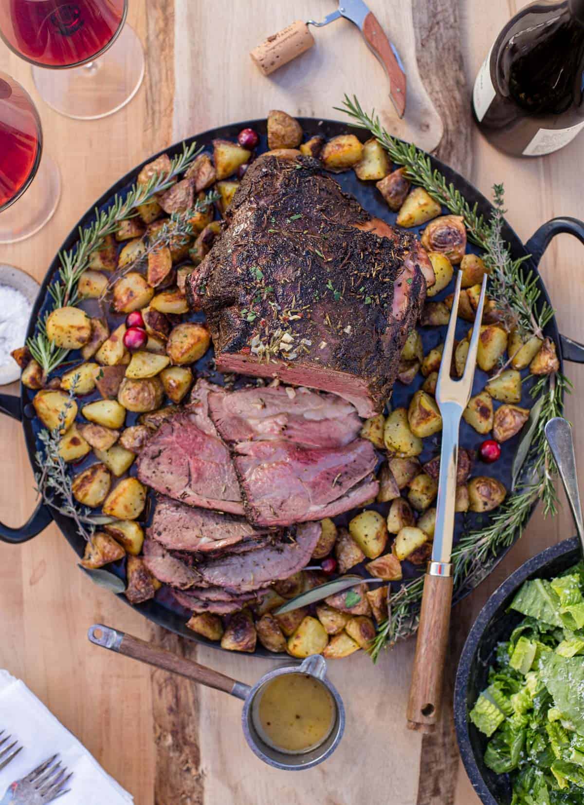 A bone in Smoked Leg of Lamb on a platter with roasted potatoes