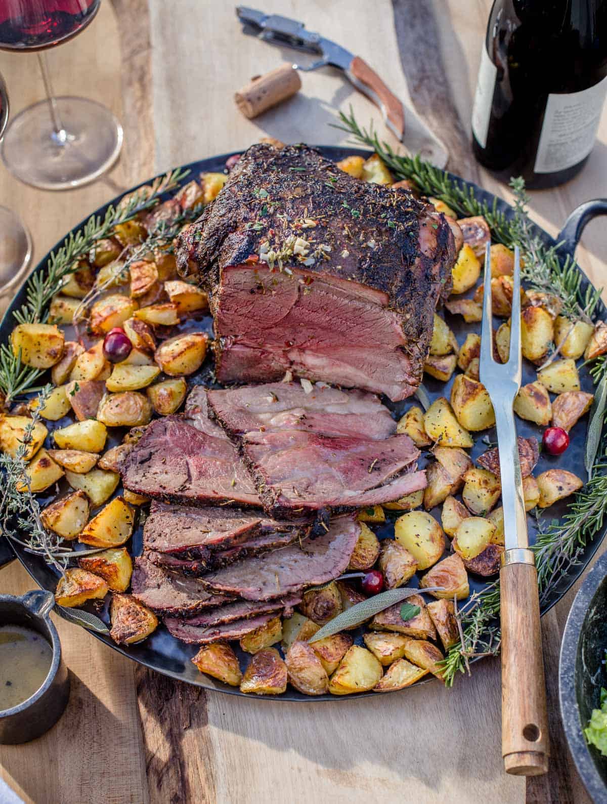 Slices of smoked leg of lamb on a platter with roasted potatoes