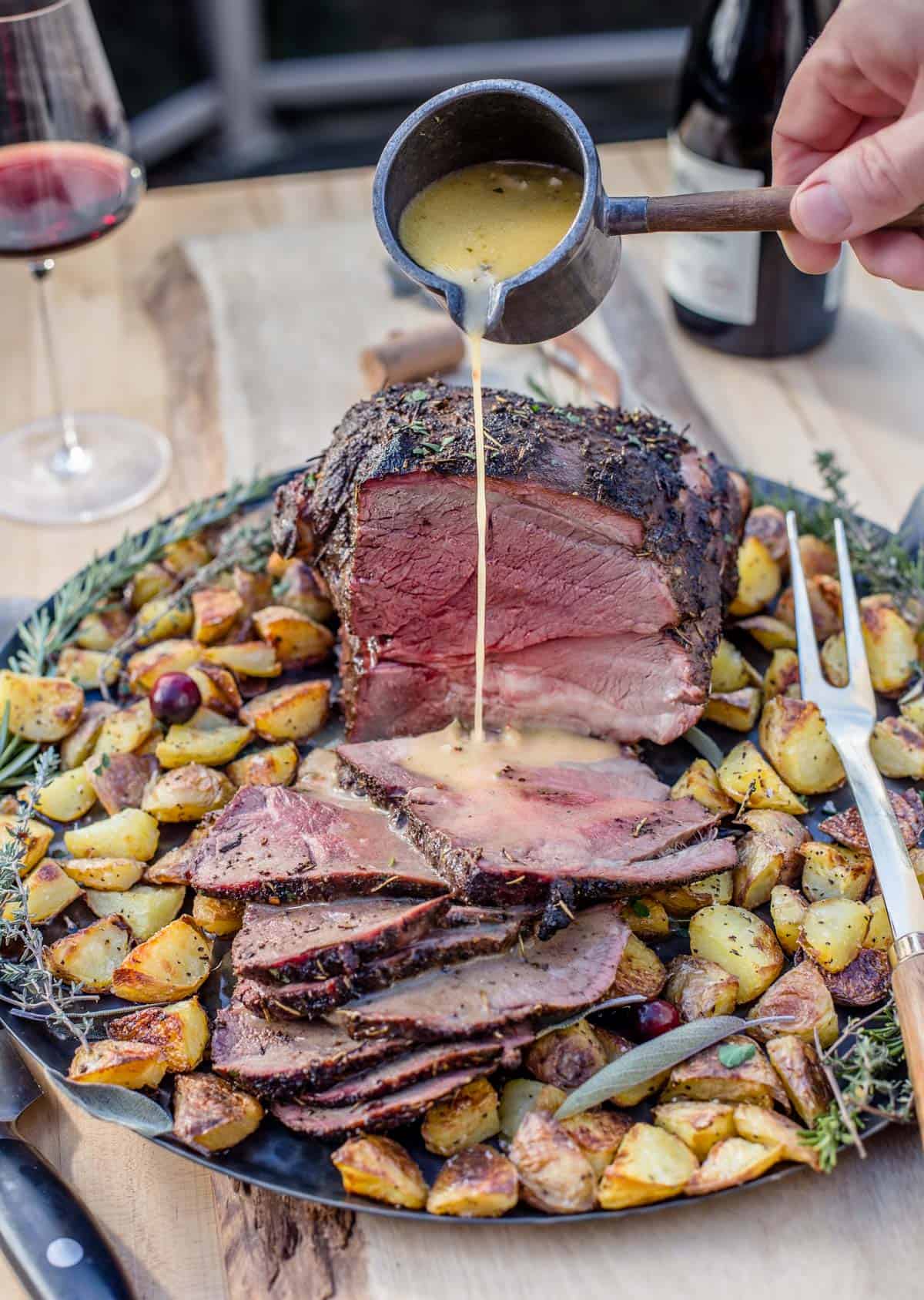 Garlic butter sauce being poured over a smoked leg of lamb