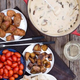 Cheese fondue platter with bread, tomatoes, and potatoes for dipping