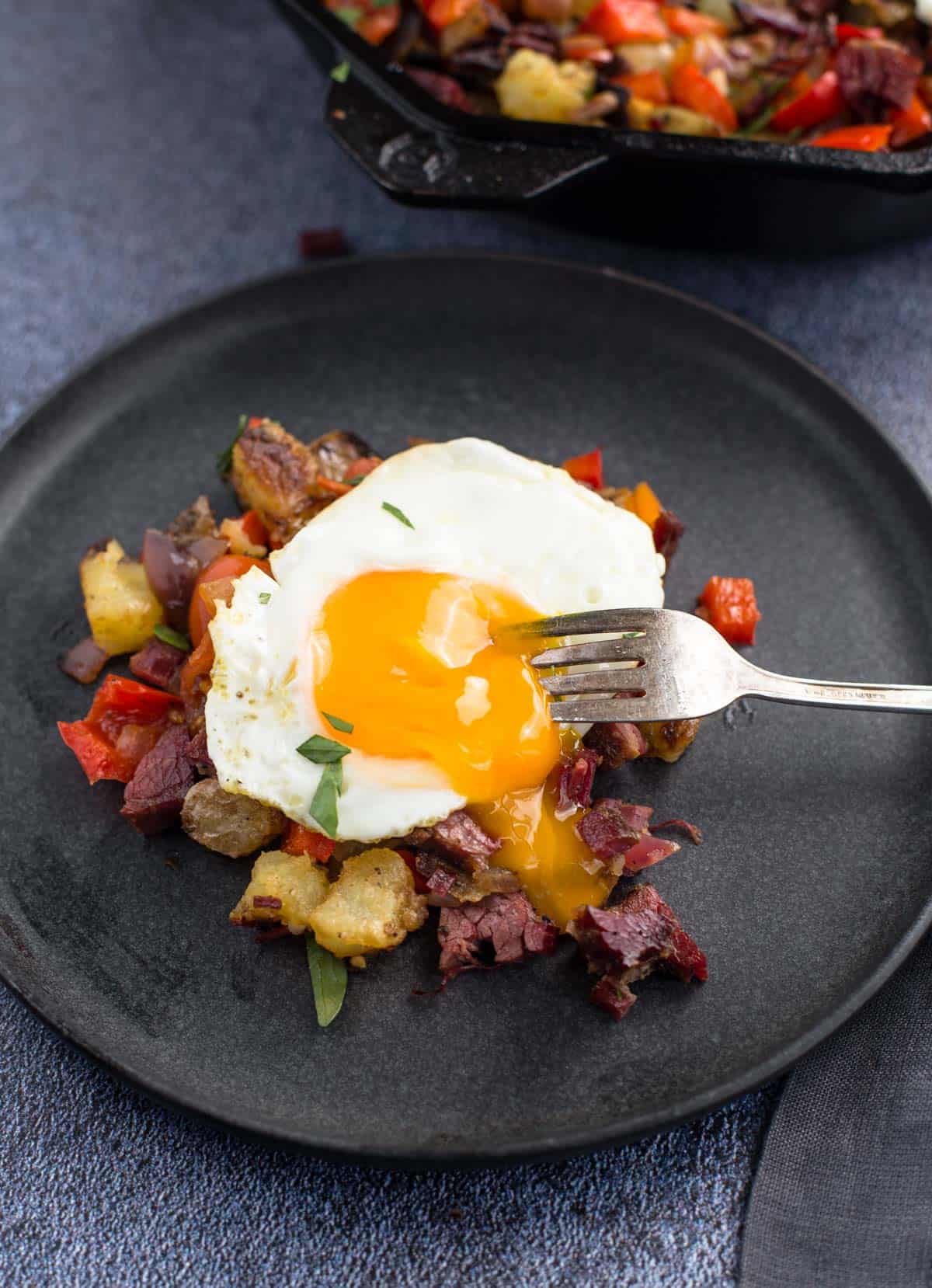 Egg sunny side up over corned beef hash on a small plate.