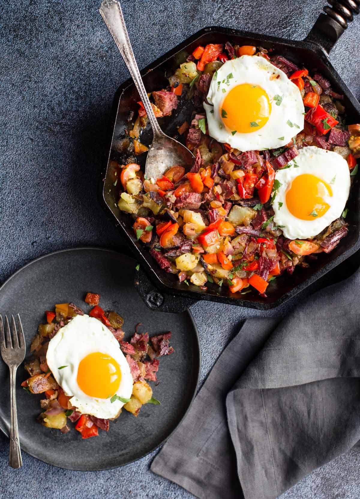 Eggs Sunnyside up over corned beef hash on a plate and cast iron skillet.